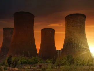 Exterior of huge cooling towers located in contemporary atomic power plant against bright setting sun under dramatic dark sky